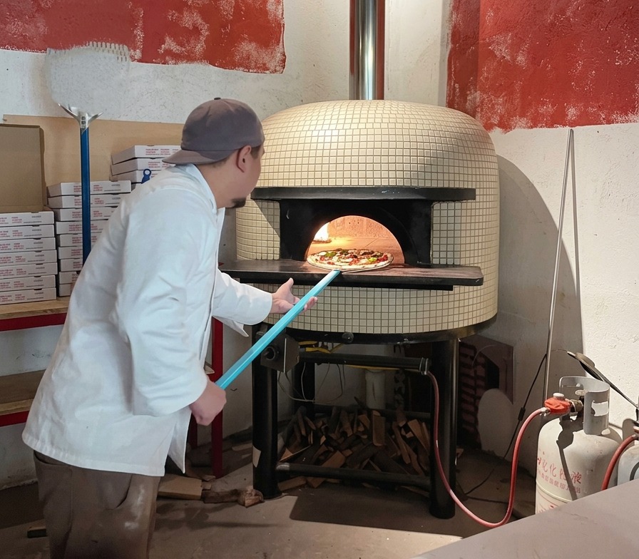 Ein Koch schiebt die Pizza mit einem blauen Pizzaschieber in einen glühend heißen Steinofen.