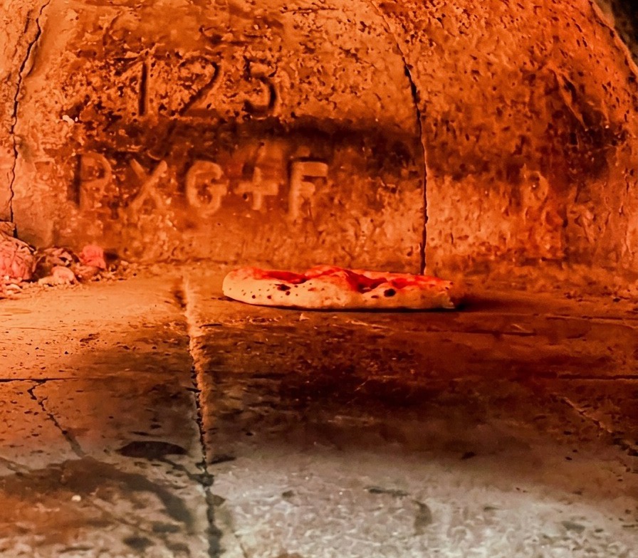 Eine neapolitanische Pizza backt im heißen Holzofen, der Rand wirft bereits Blasen.