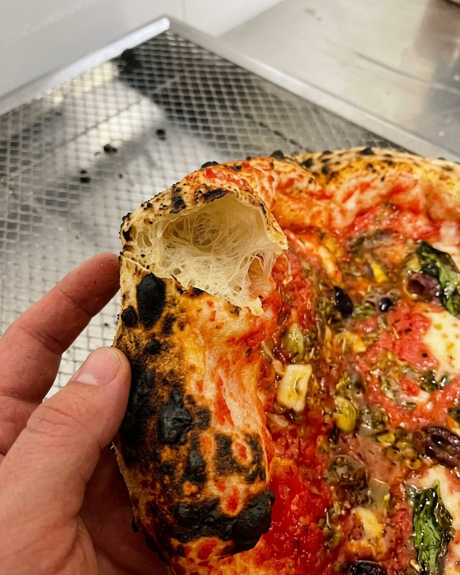 Nahaufnahme einer Hand, die ein Stück des luftigen Pizzarandes aufbricht, um die großporige Struktur zu zeigen.