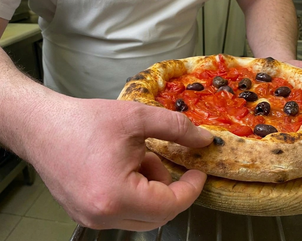 Ein Finger drückt in den luftigen, gebräunten Rand einer frisch gebackenen Pizza.