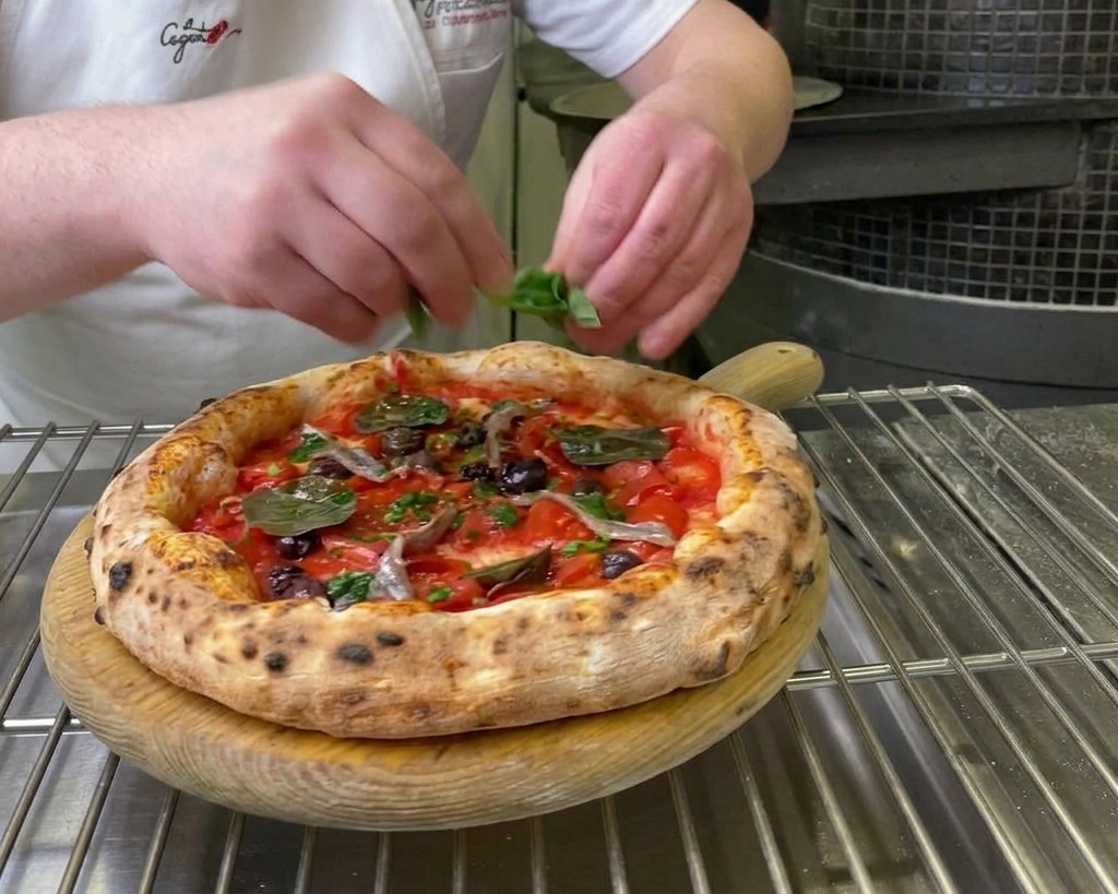 Frische grüne Basilikumblätter werden auf die fertig gebackene Pizza gelegt.