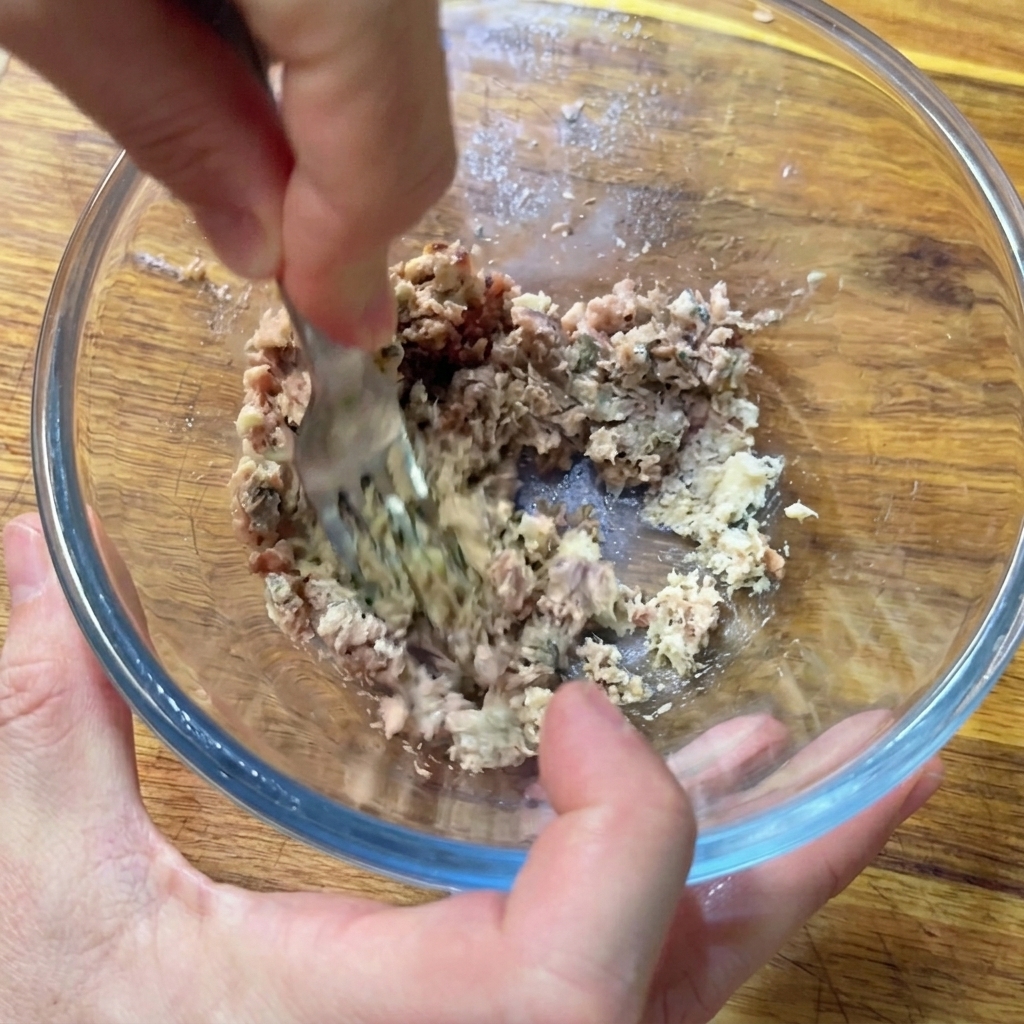 Mit einer Gabel werden Sardellen und Sardinen in einer Glasschüssel zu einer Paste zerdrückt.