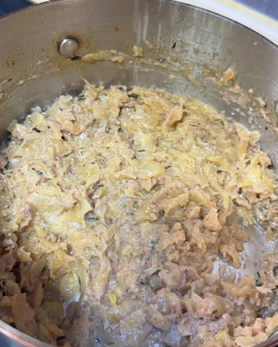 Karamellisierte Zwiebeln mit Fischpaste und Thymianspuren in einem Topf.