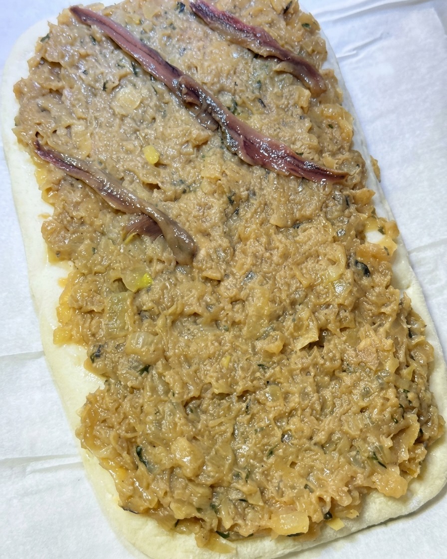 Sardellenfilets werden in einem Rautenmuster auf die Zwiebelschicht gelegt.