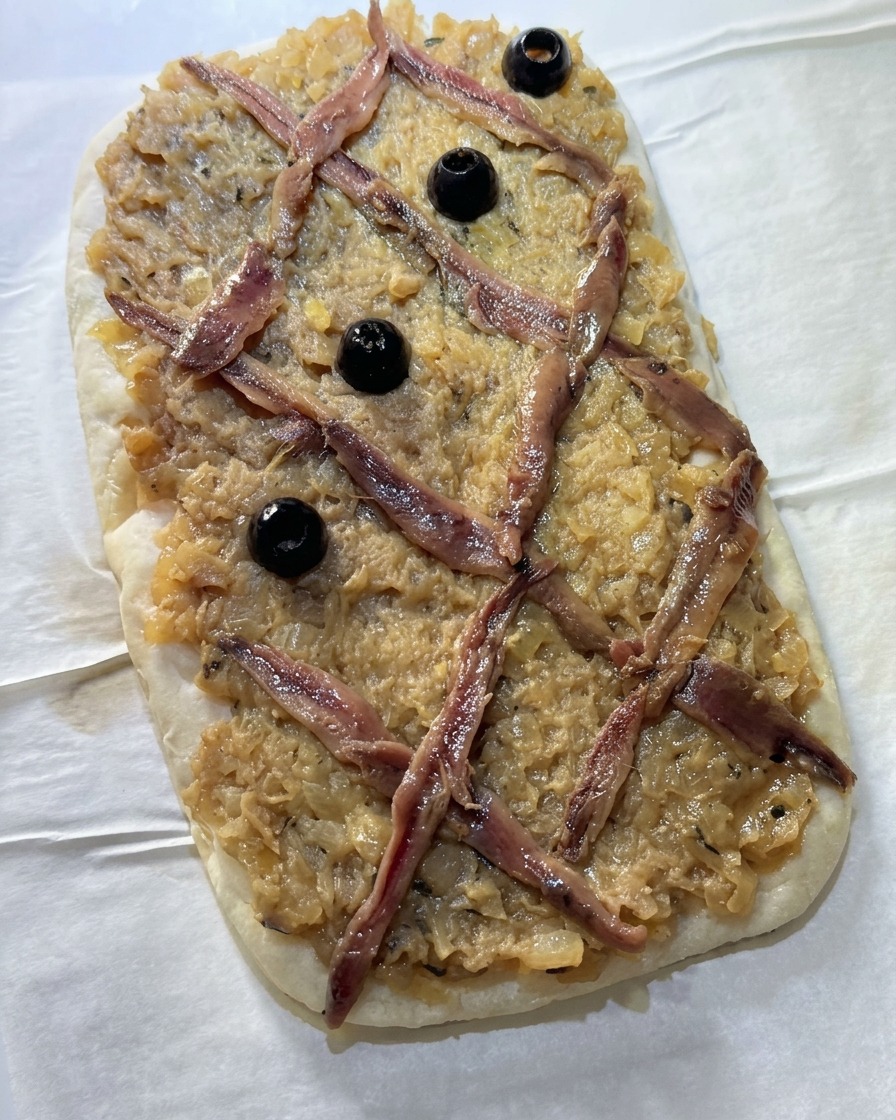 Schwarze Oliven werden in die Mitte der Sardellen-Rauten auf dem Fladenbrot gesetzt.