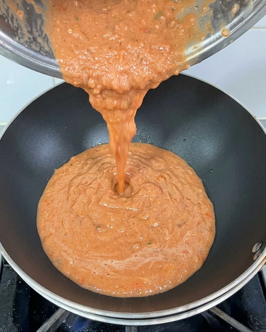 Eingießen der dickflüssigen roten Tomatensauce aus einem Metalltopf in einen heißen schwarzen Wok.