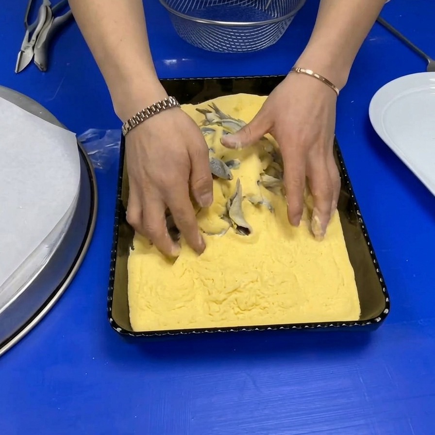 Hände wenden frische ganze Sardellen in einer Schale mit leuchtend gelbem Maismehl.