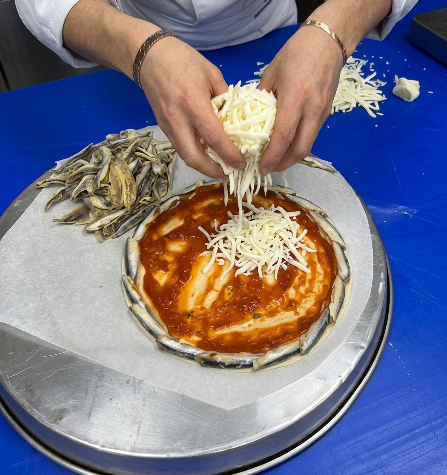 Hände streuen großzügig frisch geriebenen Käse auf den mit Sauce bestrichenen Pizzaboden.