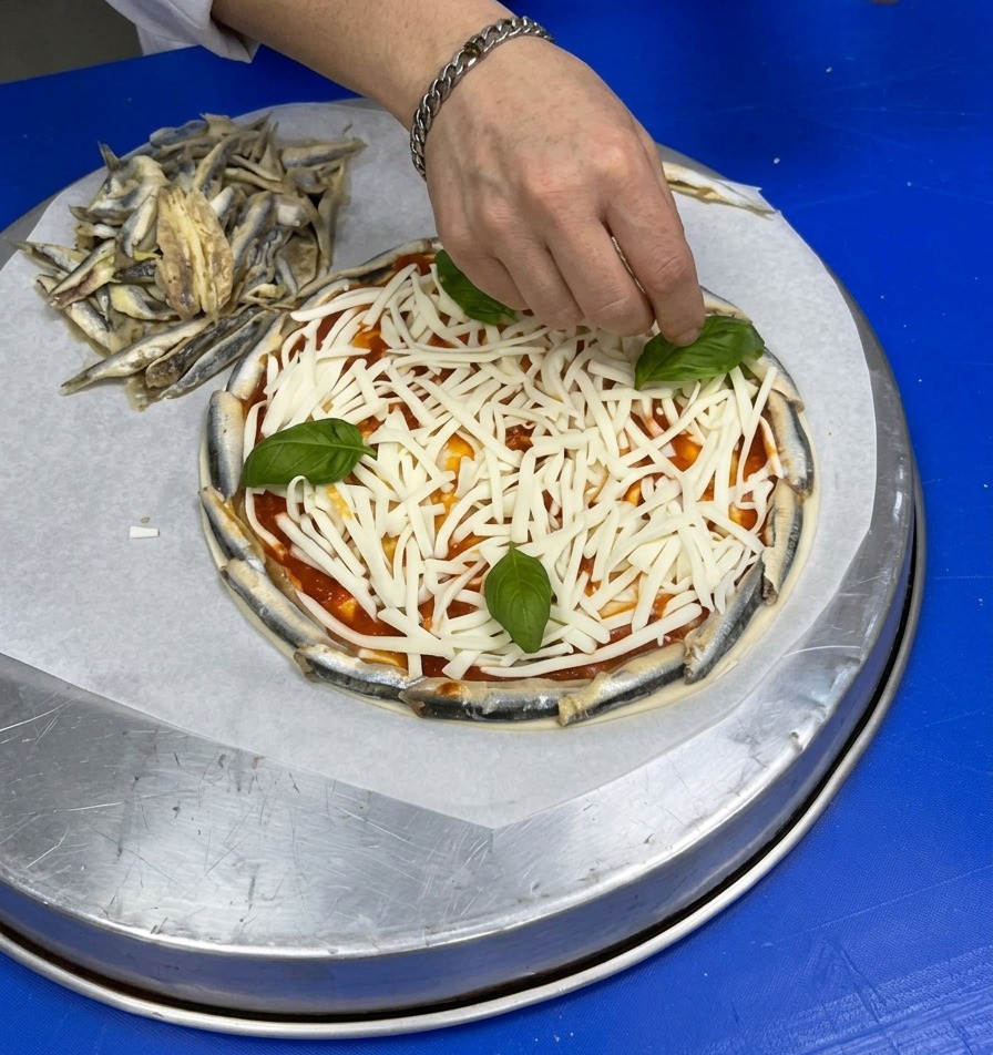 Eine Hand legt ganze frische Basilikumblätter auf die Schicht aus geriebenem Käse.