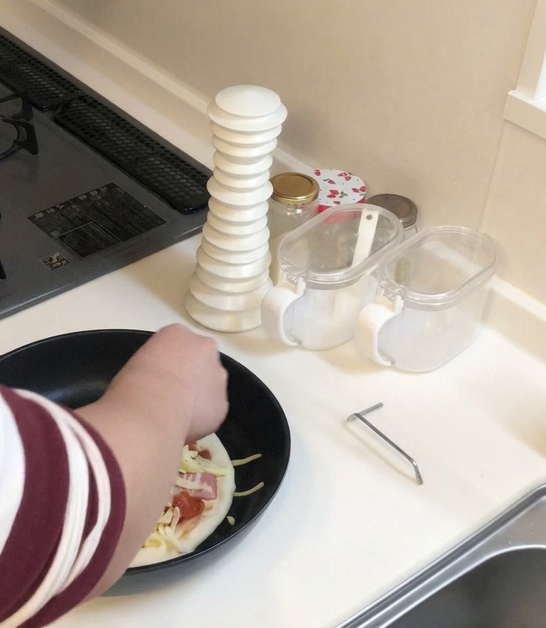 Eine Person streut eine Handvoll geriebenen Käse über die belegte Pizza.