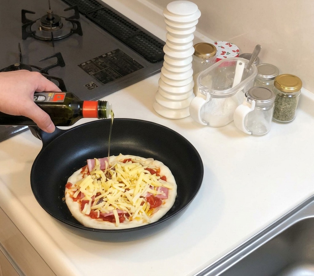 Olivenöl wird über die mit Käse belegte Pizza in der Pfanne geträufelt.