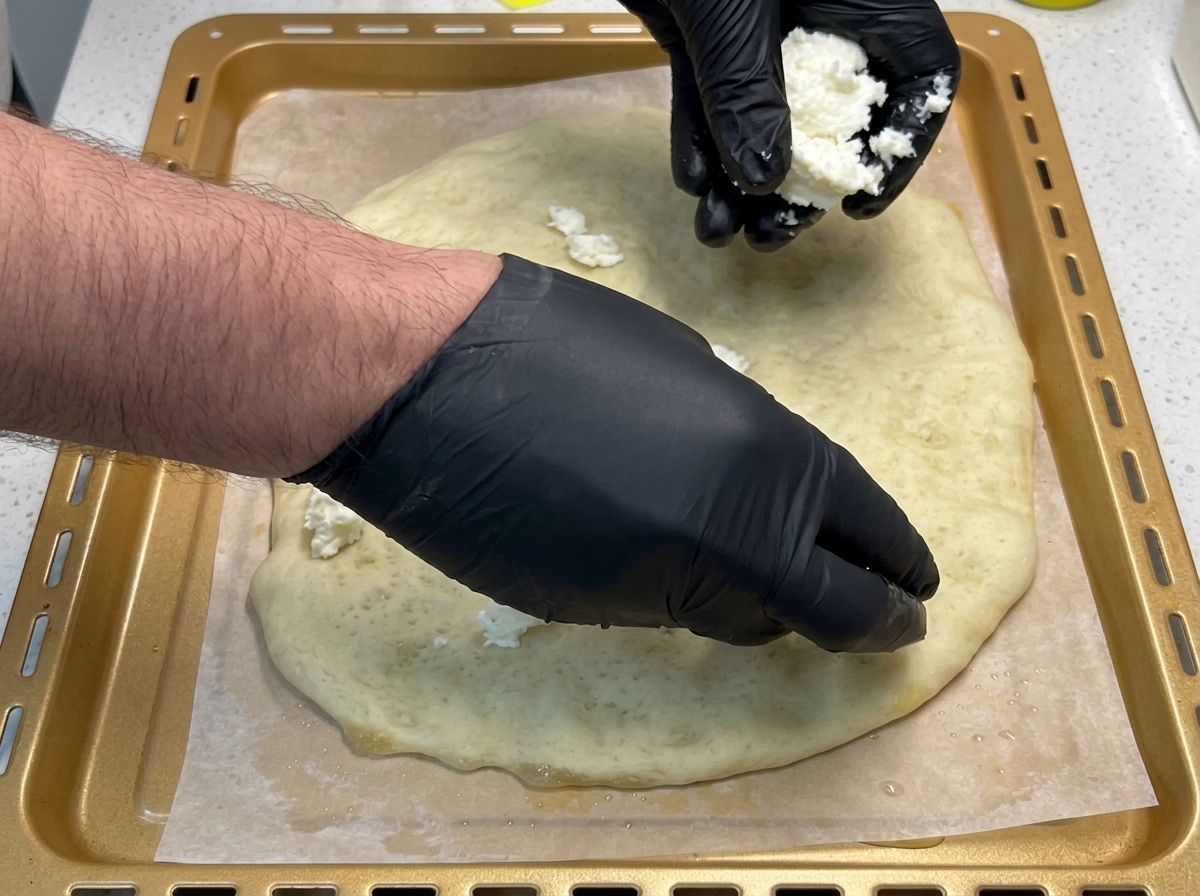 Hände legen gezupfte Stücke Mozzarella auf einen goldbraun vorgebackenen Pizzateig.