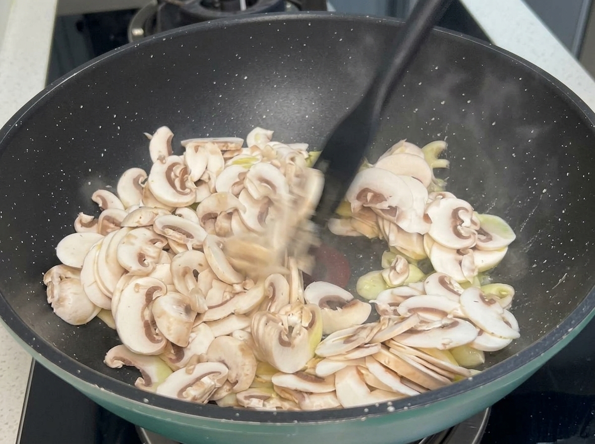 Champignonscheiben und Knoblauchzehen werden mit einem schwarzen Spatel in einer heißen Pfanne gerührt.
