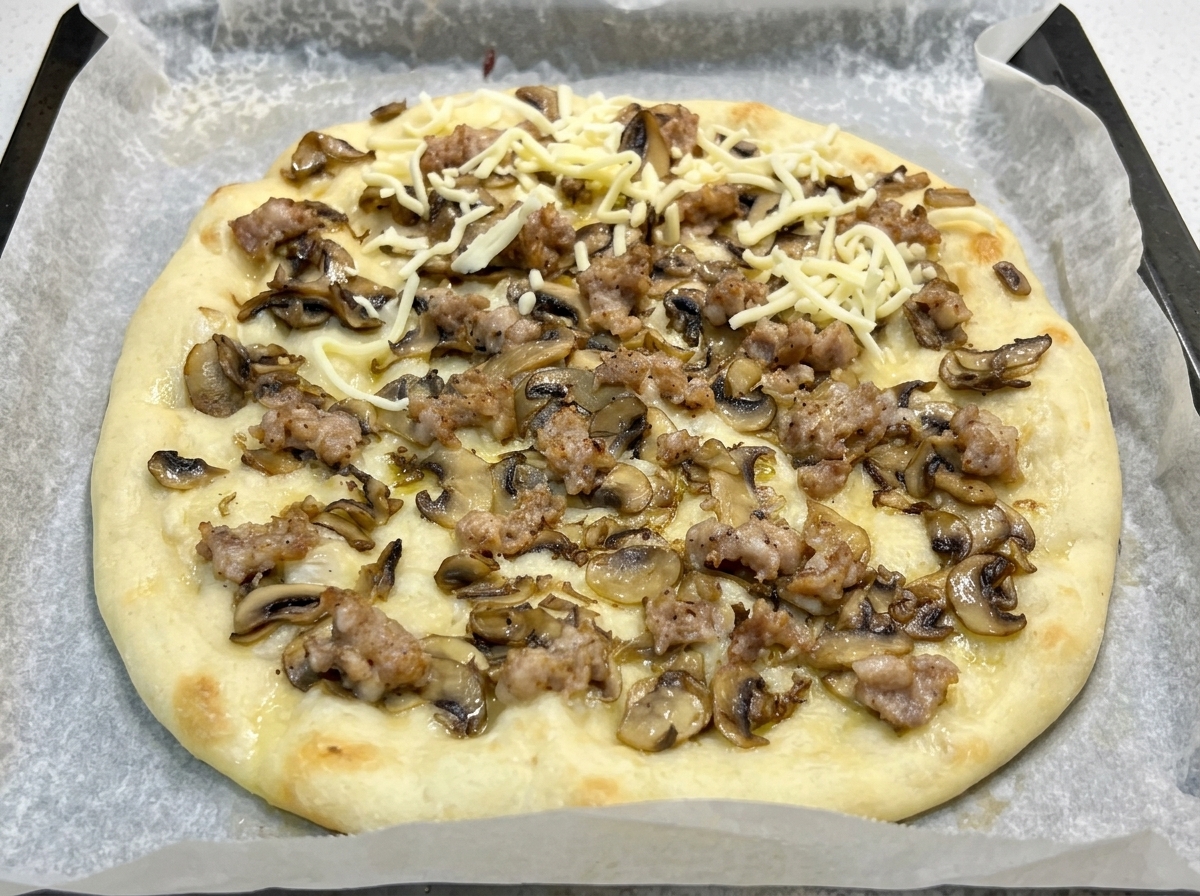 Eine vorgebackene Pizza mit Pilzen und Salsiccia wird mit geriebenem Mozzarella bestreut.