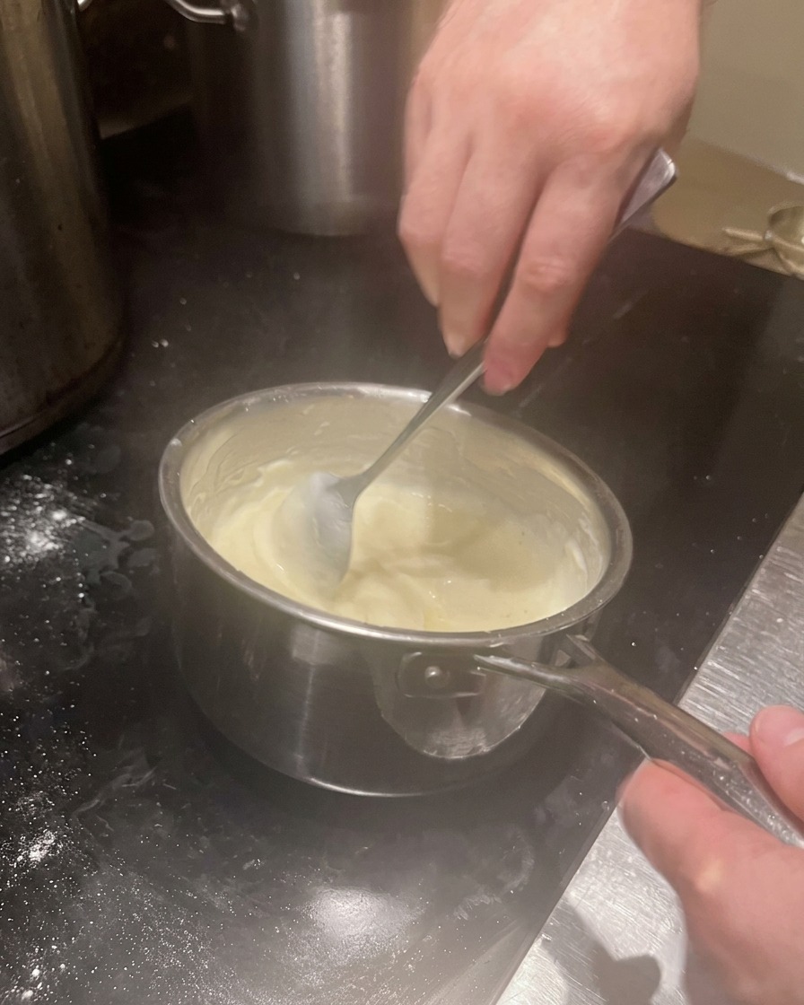 Eine cremige, eingedickte weiße Sauce wird im Topf umgerührt.