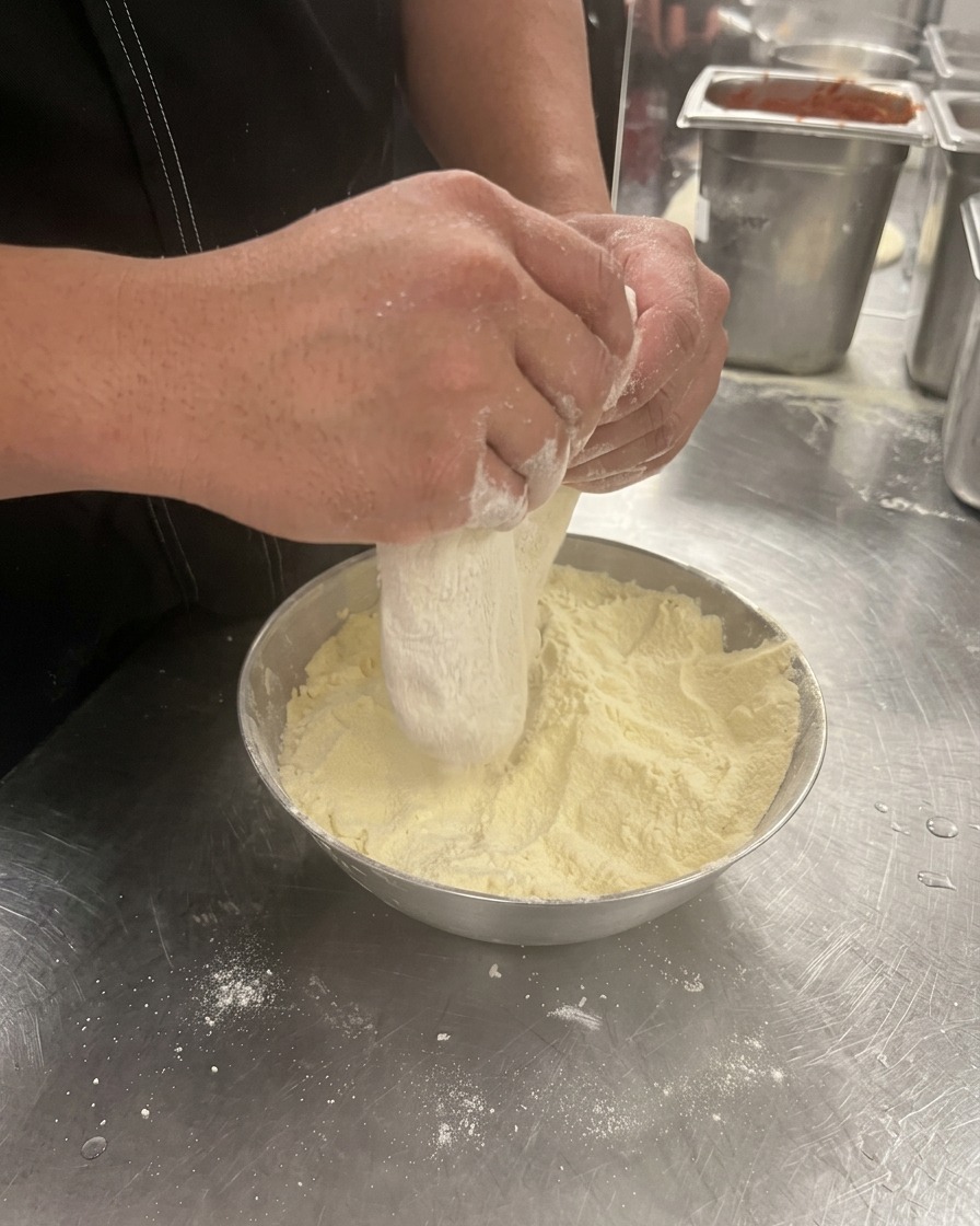 Hände drücken und dehnen eine Kugel Pizzateig in einer Schüssel mit Mehl.