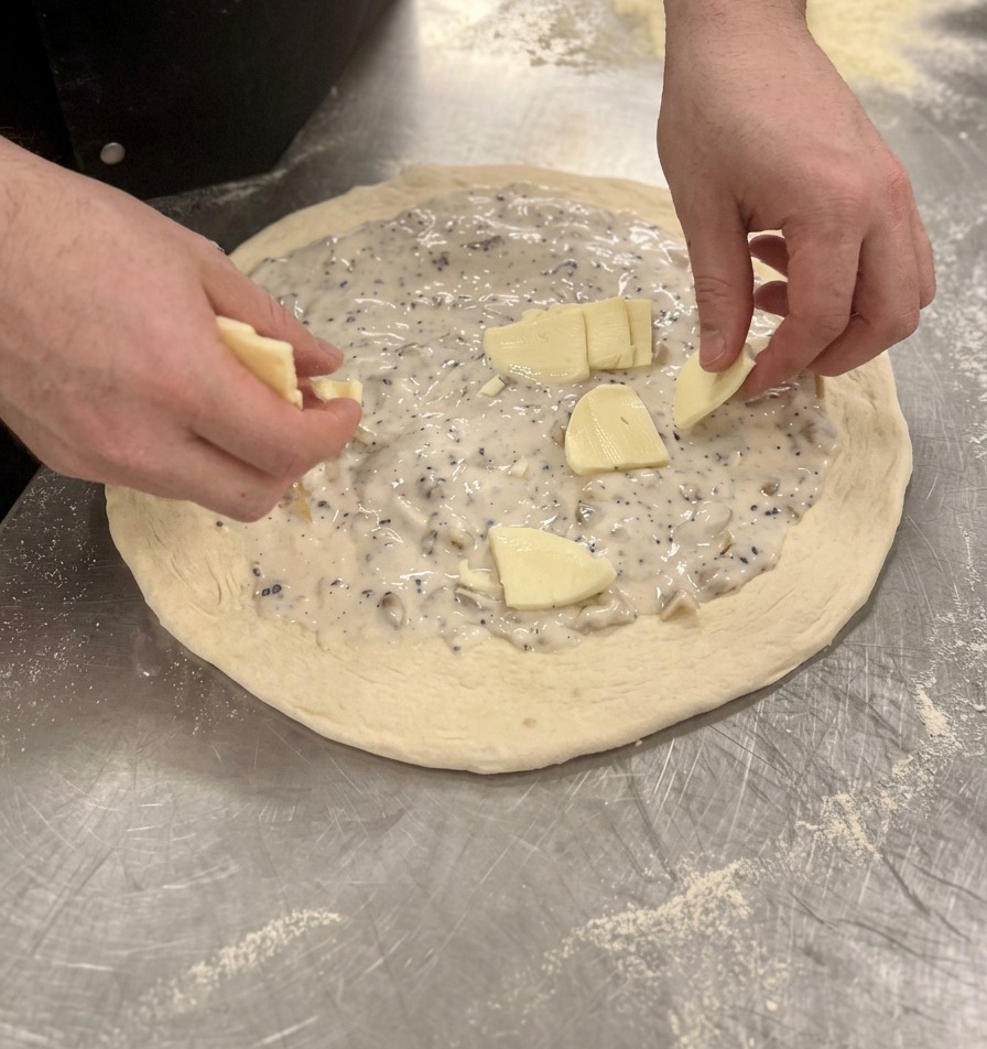 Hände verteilen Mozzarellastücke gleichmäßig auf der Pilzsauce der Pizza.