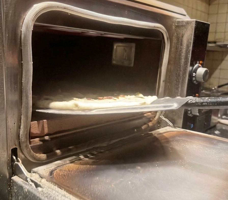 Die belegte Pizza wird mit einem Pizzaschieber in einen heißen Ofen geschoben.