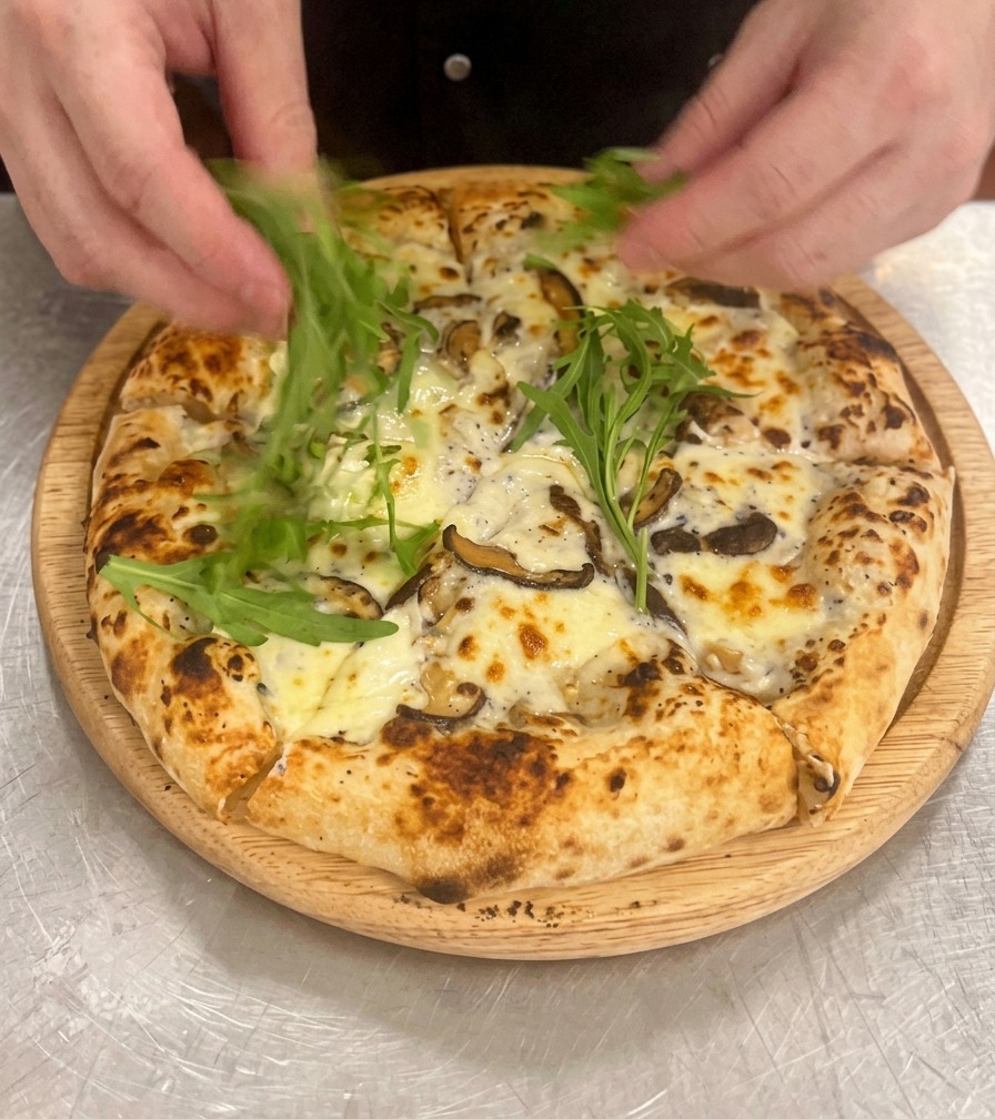Grüner Rucola wird auf der frisch gebackenen und geschnittenen Pizza verteilt.