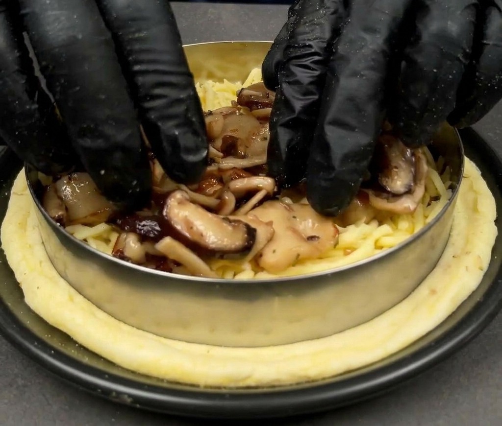 Hände legen gebratene Pilze auf die Mozzarella-Schicht einer Pizza.