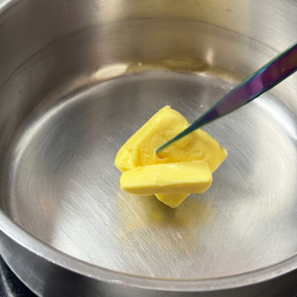 Ein quadratisches Stück gelbe Butter schmilzt in einem glänzenden Edelstahltopf.
