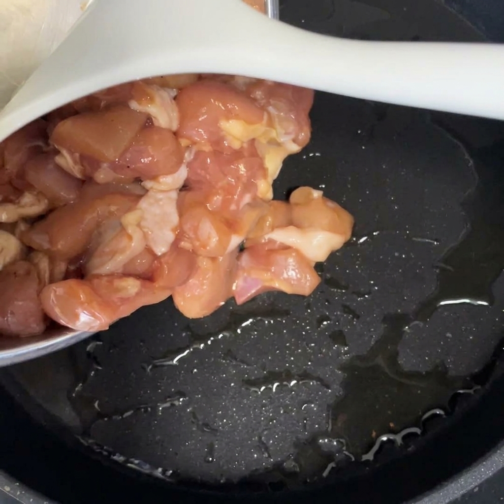 Rohe marinierte Hähnchenstücke werden in eine schwarze Pfanne mit heißem Öl gegeben.