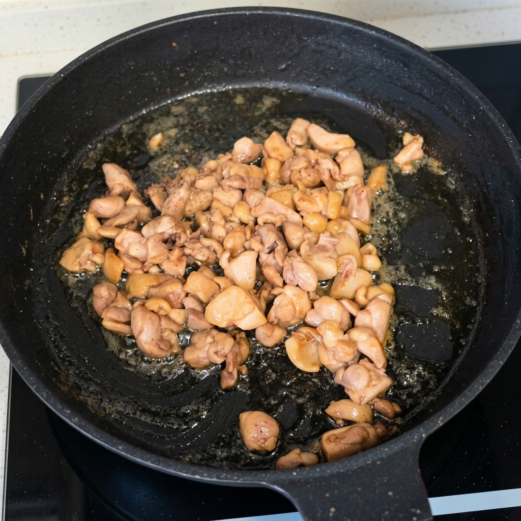 Gegarte und gebräunte Hähnchenstücke werden in einer schwarzen Pfanne gebraten.