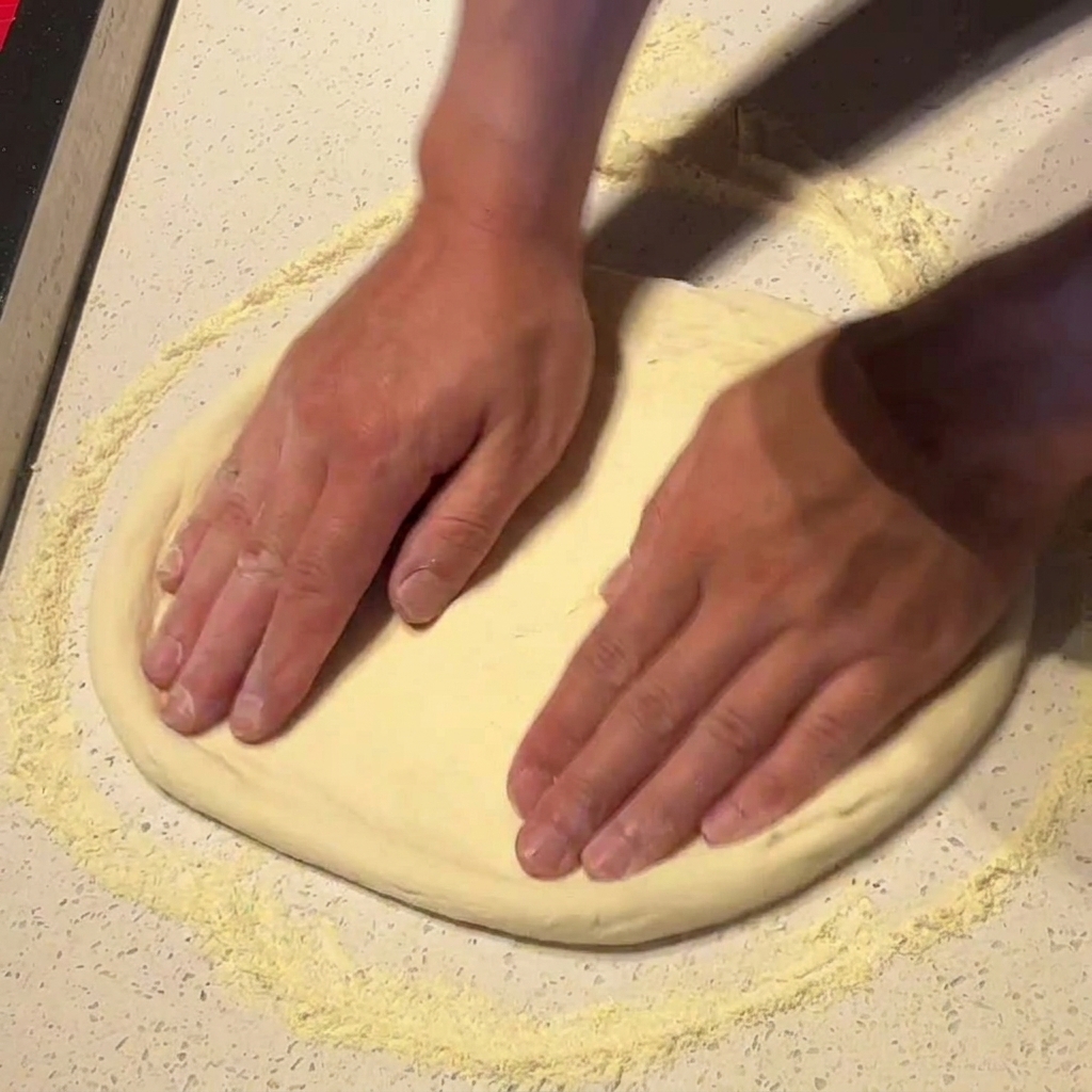 Hände dehnen den Pizzateig vorsichtig auf einer bemehlten Fläche in eine runde Form.