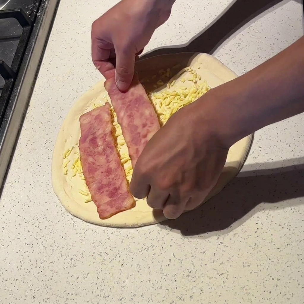 Hände legen breite Streifen von leicht vorgekochtem Speck auf die Pizza.