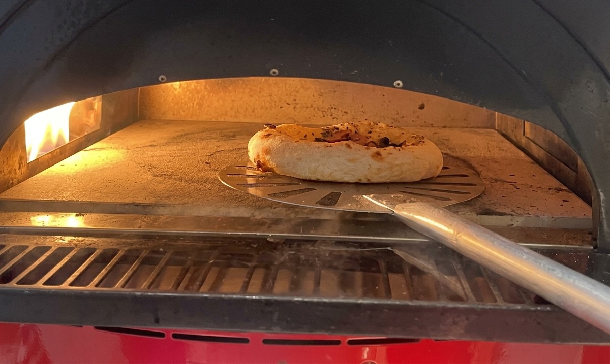 Eine kleine Pizza mit Pilzen und Wurst, die im heißen Ofen backt, während der Rand deutlich aufgeht.