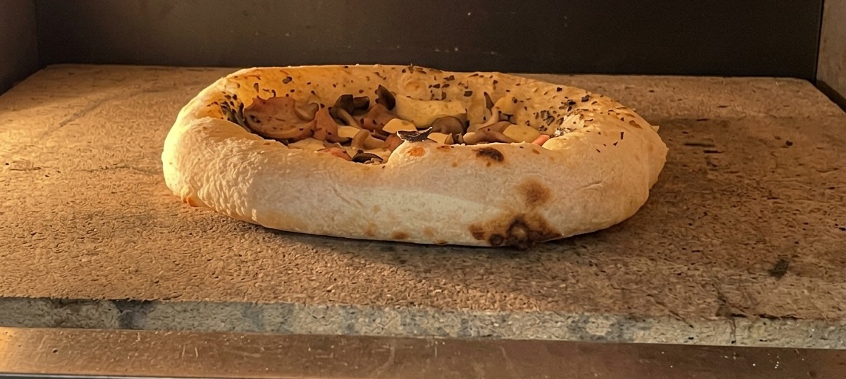 Eine fertig gebackene Pizza im Ofen mit deutlich aufgegangenem und leicht gebräuntem Rand.