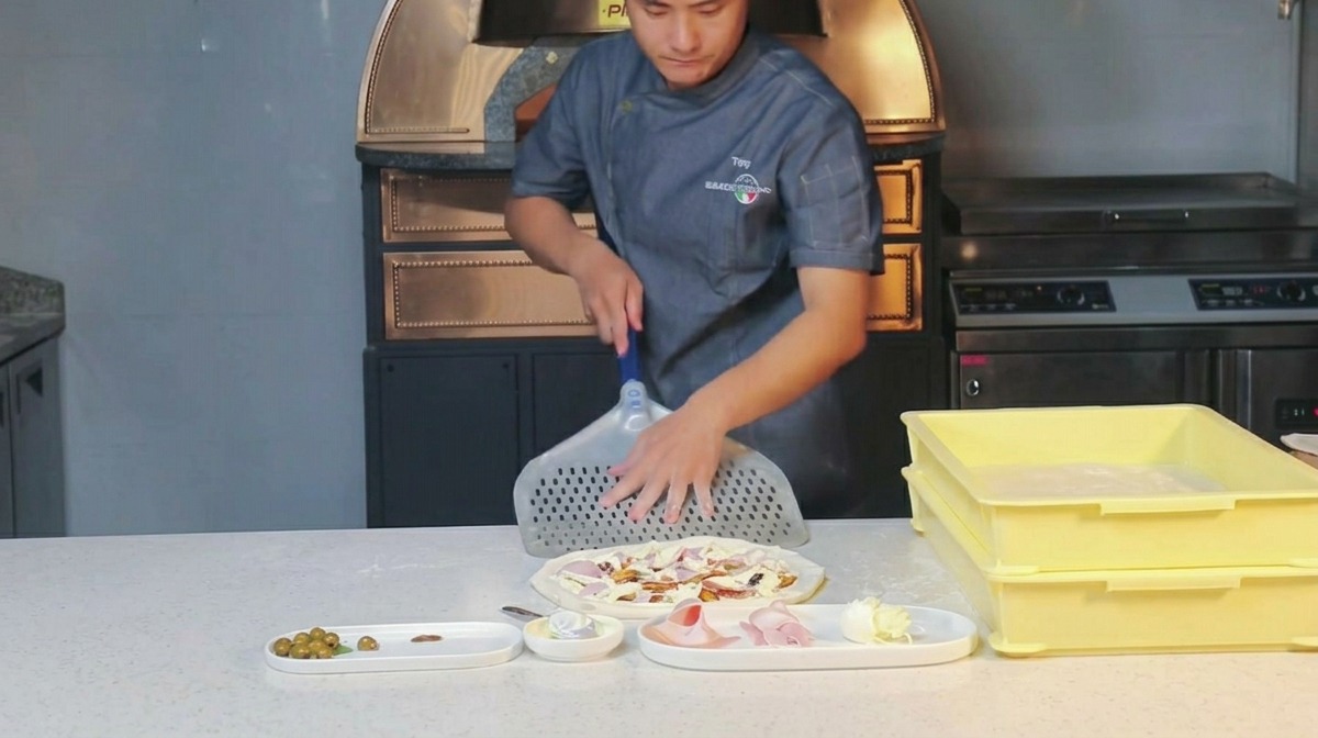 Ein Koch bestäubt eine perforierte Pizzaschaufel aus Metall mit Mehl.