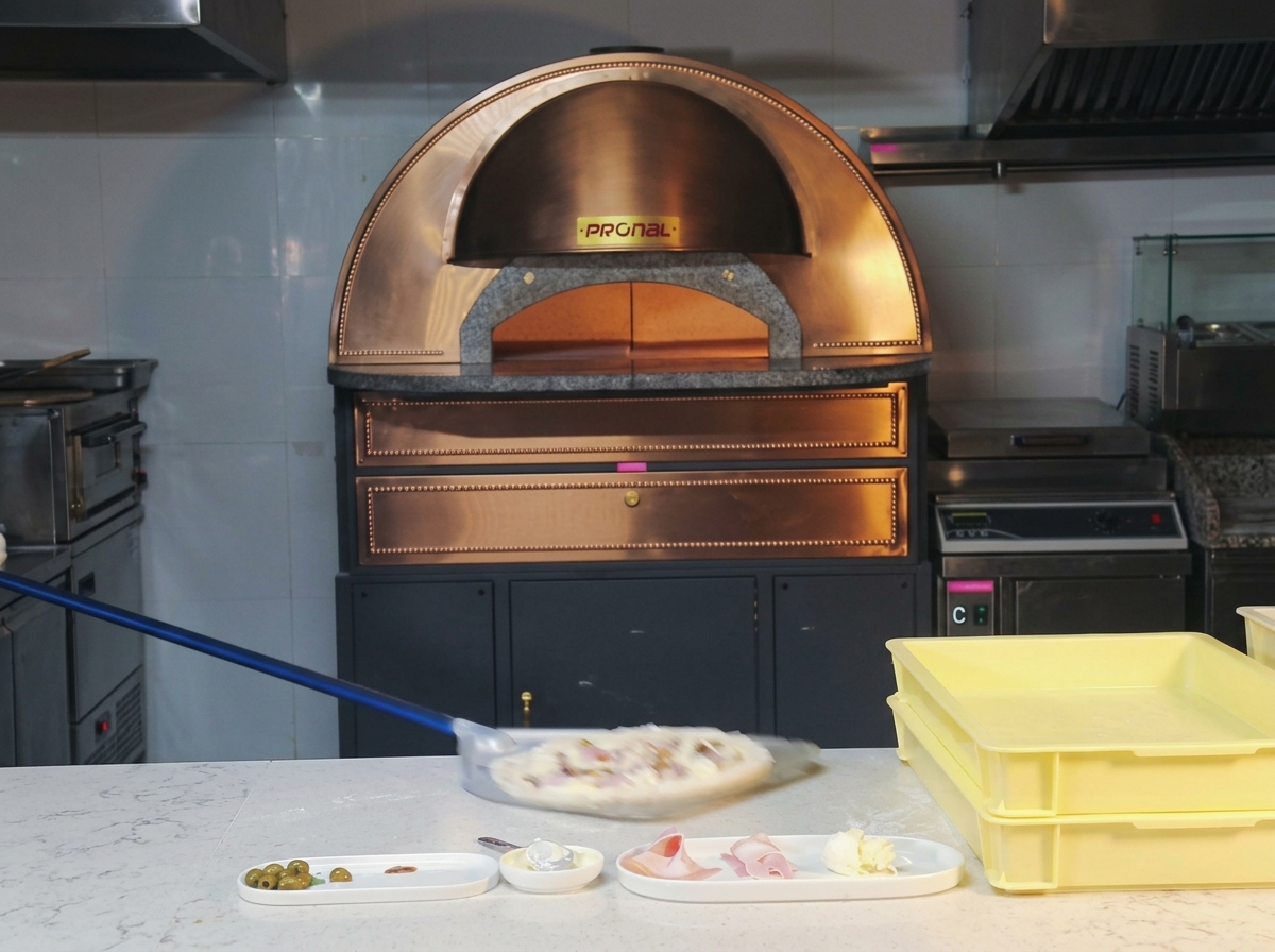 Eine Pizza wird auf einer Metallschaufel in einen glühenden Steinofen geschoben.