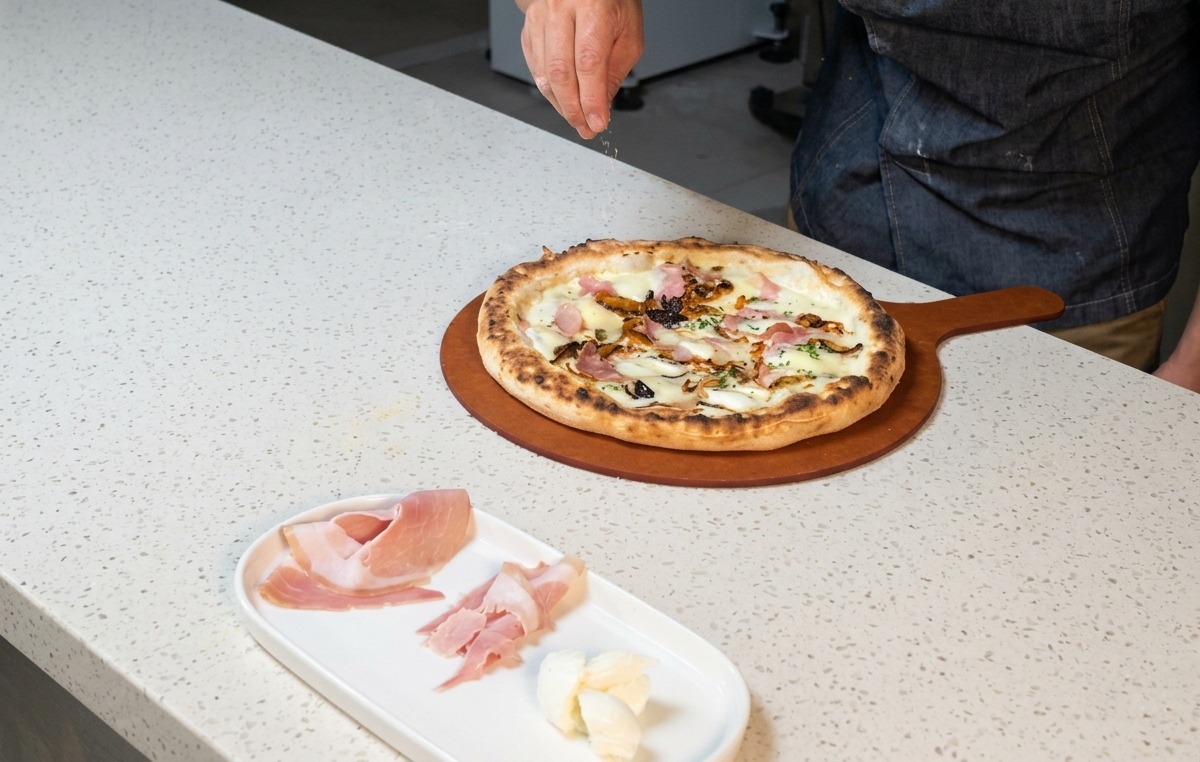 Hände streuen geriebenen Käse über die heiße, frisch gebackene Pizza.
