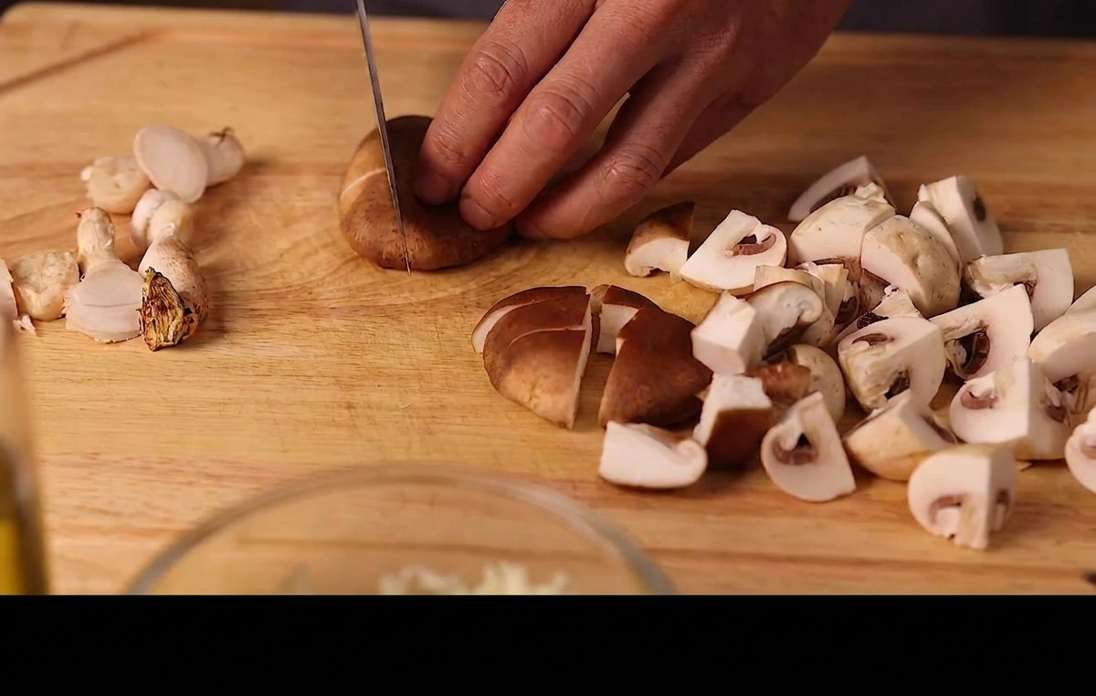 Hände schneiden frische Shiitake und Champignons auf einem Holzschneidebrett in Stücke.
