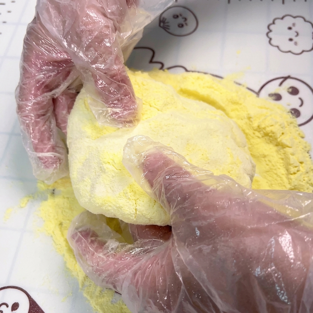 Hände drücken und dehnen ein rundes Teigstück auf einer mit gelber Maisstärke bestreuten Fläche.