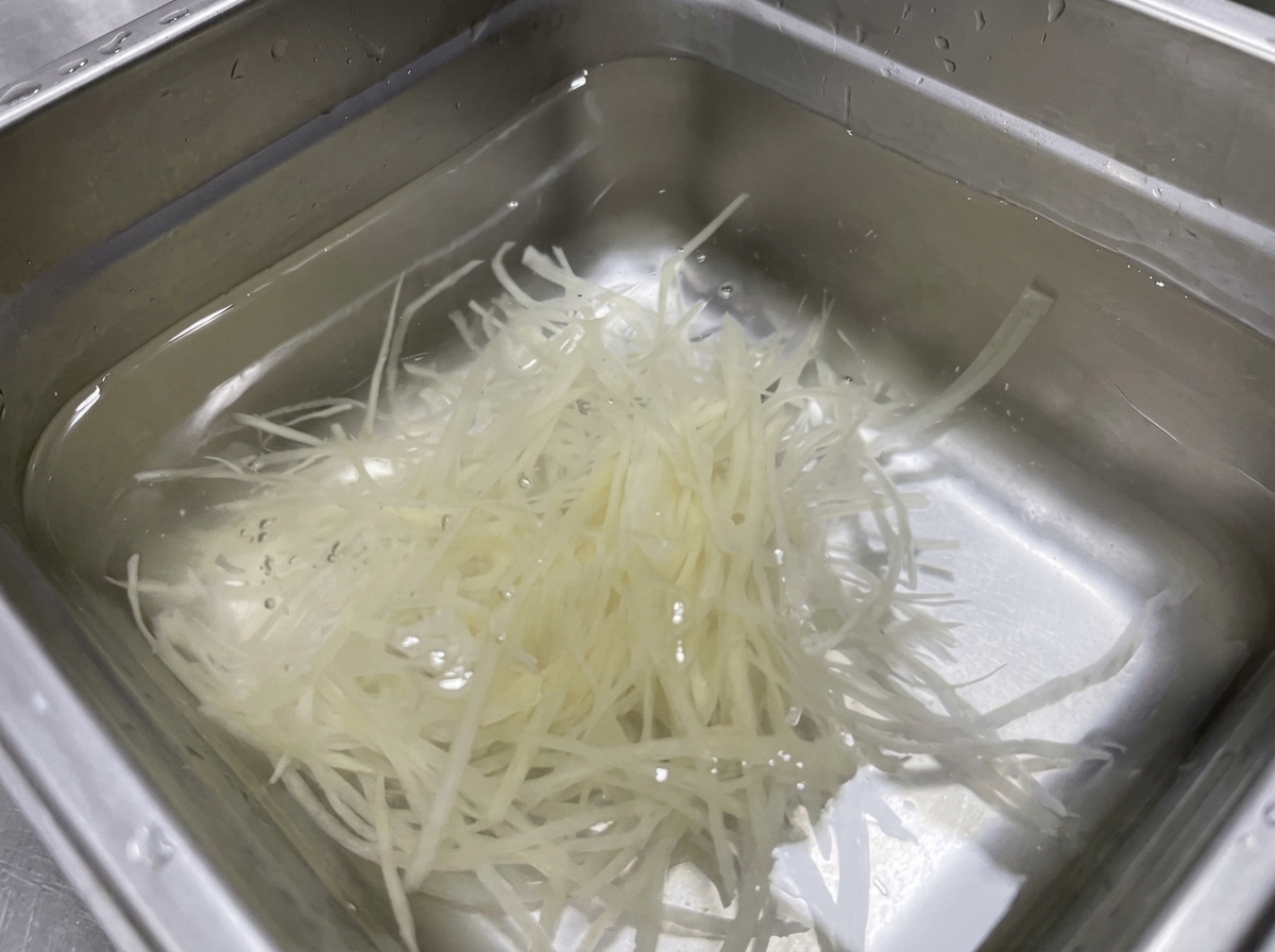 Julienne-Kartoffeln liegen in einer Edelstahlschale mit klarem Wasser.