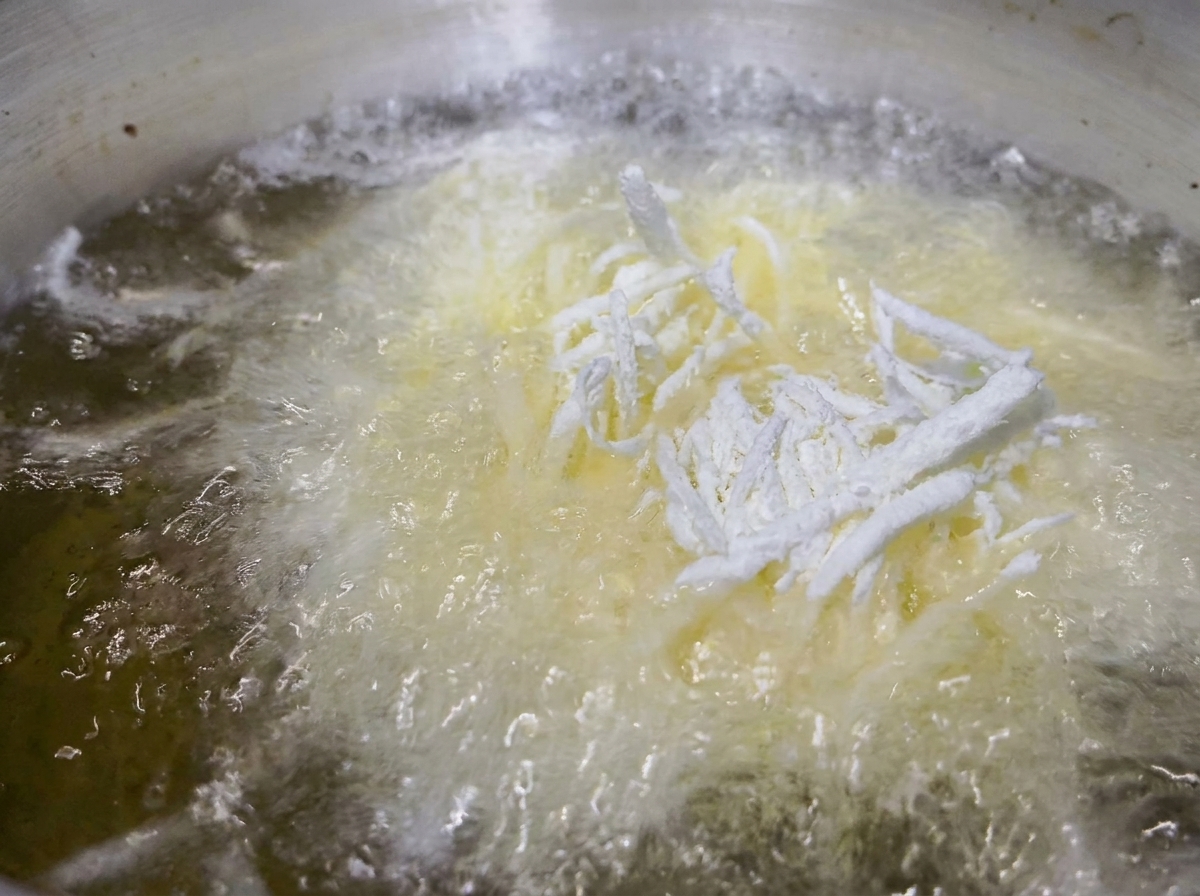 Mehlierte Kartoffelstifte frittieren in sprudelndem heißem Öl.