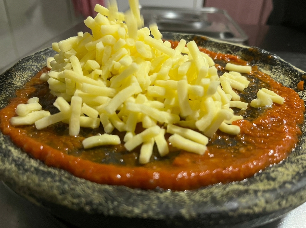 Geriebener Käse wird über die rote Sauce auf dem schwarzen Pizzaboden gestreut.
