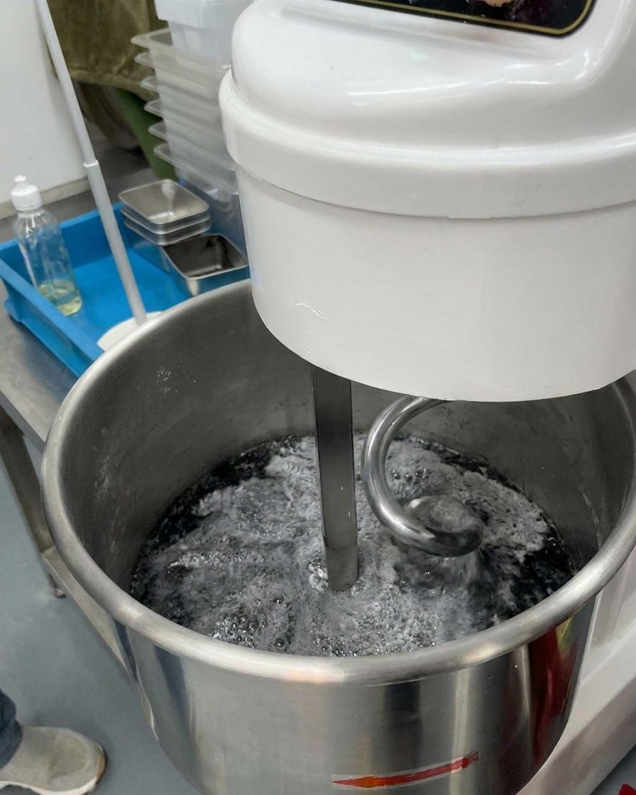 Klares Eiswasser wird in eine Rührschüssel gegossen, die eine dunkelgraue Mehlmischung enthält.