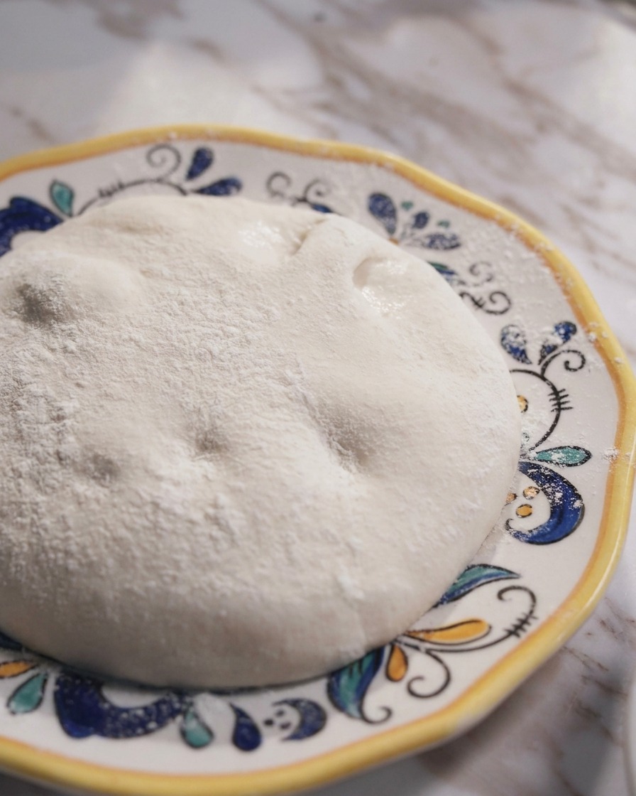 Ein glatter, runder Ball fermentierter neapolitanischer Pizzateig auf einem dekorativen Keramikteller.