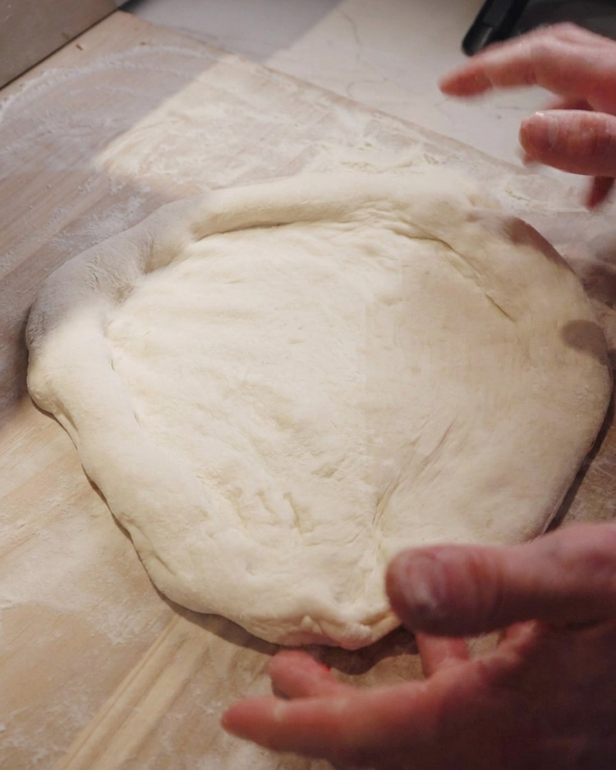 Ein Koch dehnt den Pizzateig mit der traditionellen Schlagtechnik auf einer Holztheke.