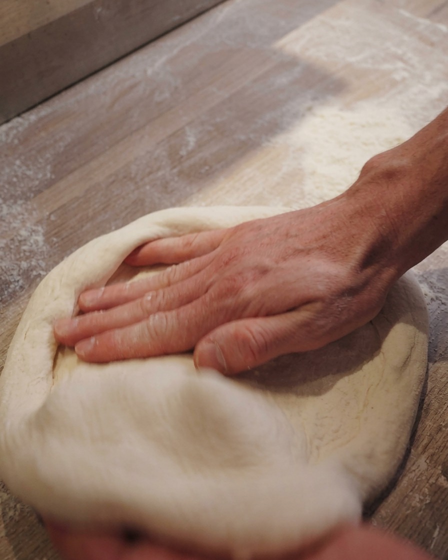 Hände ziehen einen runden Pizzateig vorsichtig in die endgültige Form auf einer bemehlten Fläche.