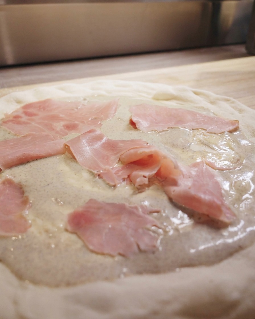 Schinkenscheiben werden locker auf der Trüffelsauce der Pizza verteilt.