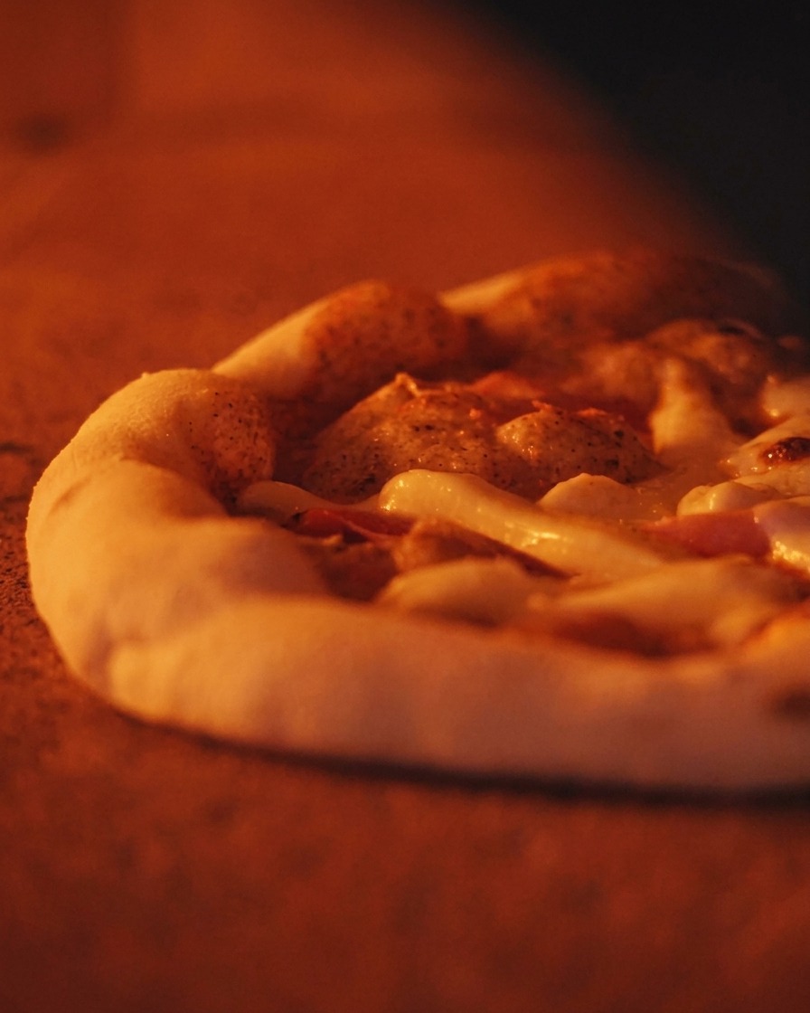 Nahaufnahme einer blubbernden Pizza mit dickem, luftigem Rand im orange leuchtenden Ofen.