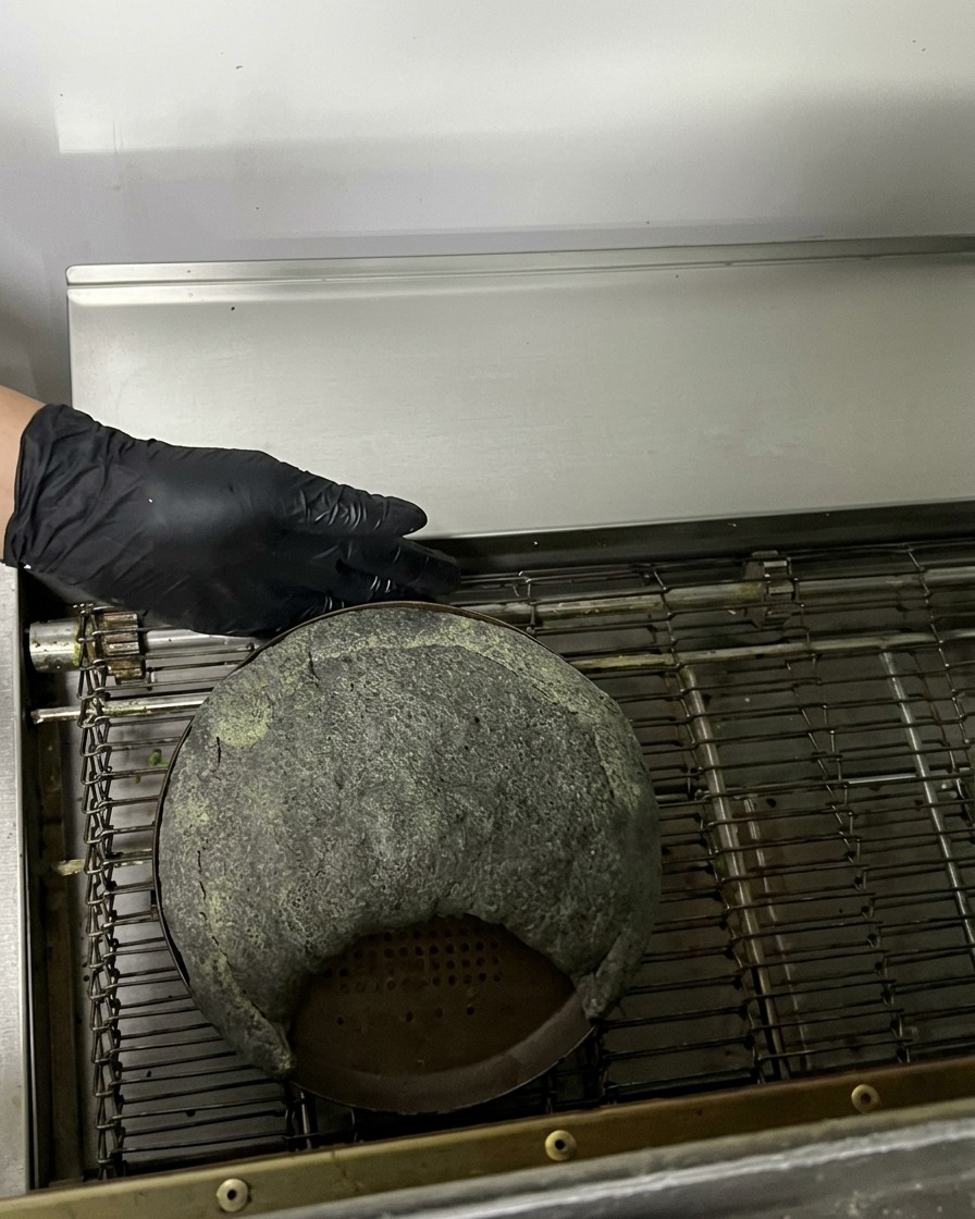 Eine rohe schwarze Calzone auf einem Metallblech fährt in einen kommerziellen Durchlaufofen.