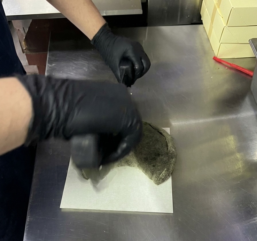 Aufschneiden einer gebackenen schwarzen Calzone mit einem Wiegemesser auf einem weißen Brett.