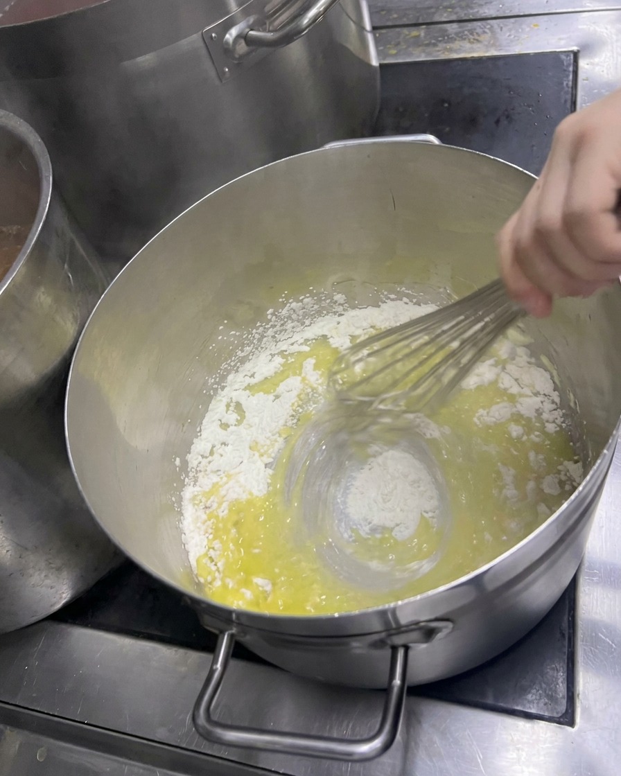Ein Schneebesen rührt Mehl in geschmolzene Butter ein, um eine helle Paste zu erzeugen.