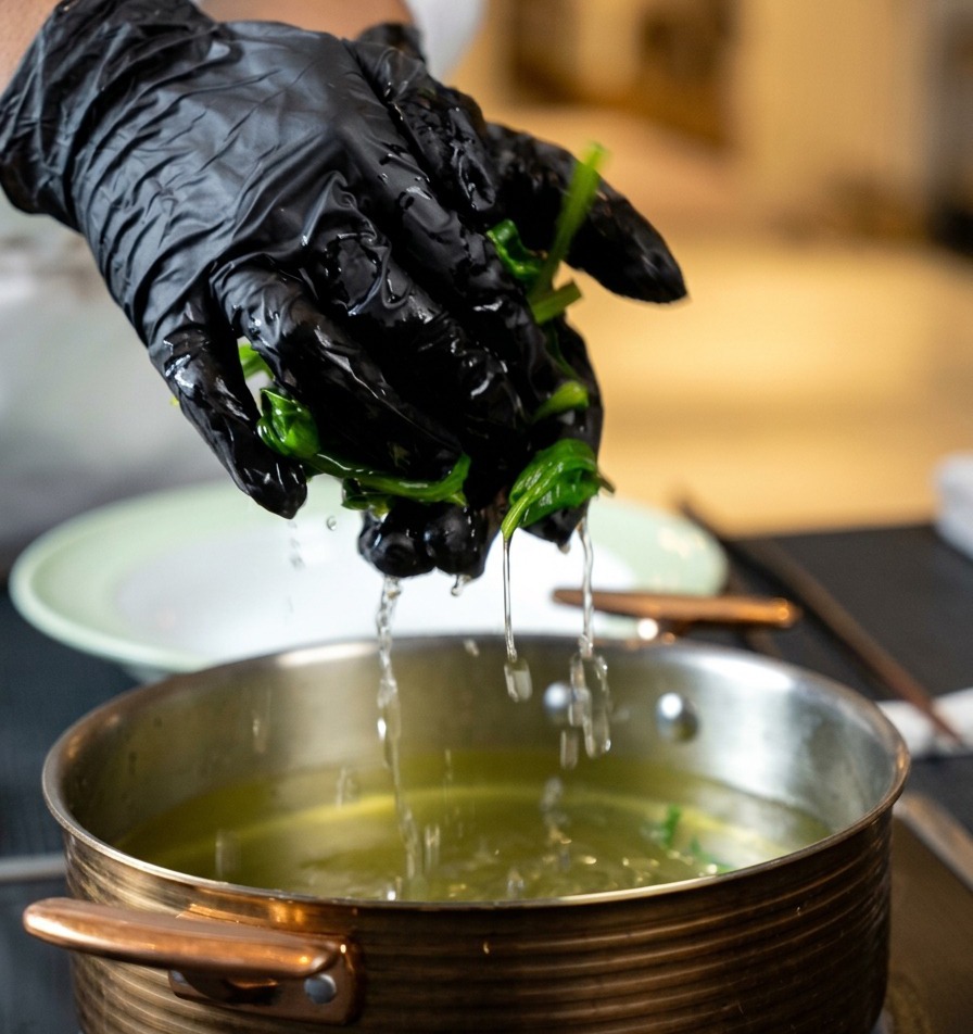Hände drücken das überschüssige Wasser aus einer Handvoll gekochtem Spinat über einem Topf aus.