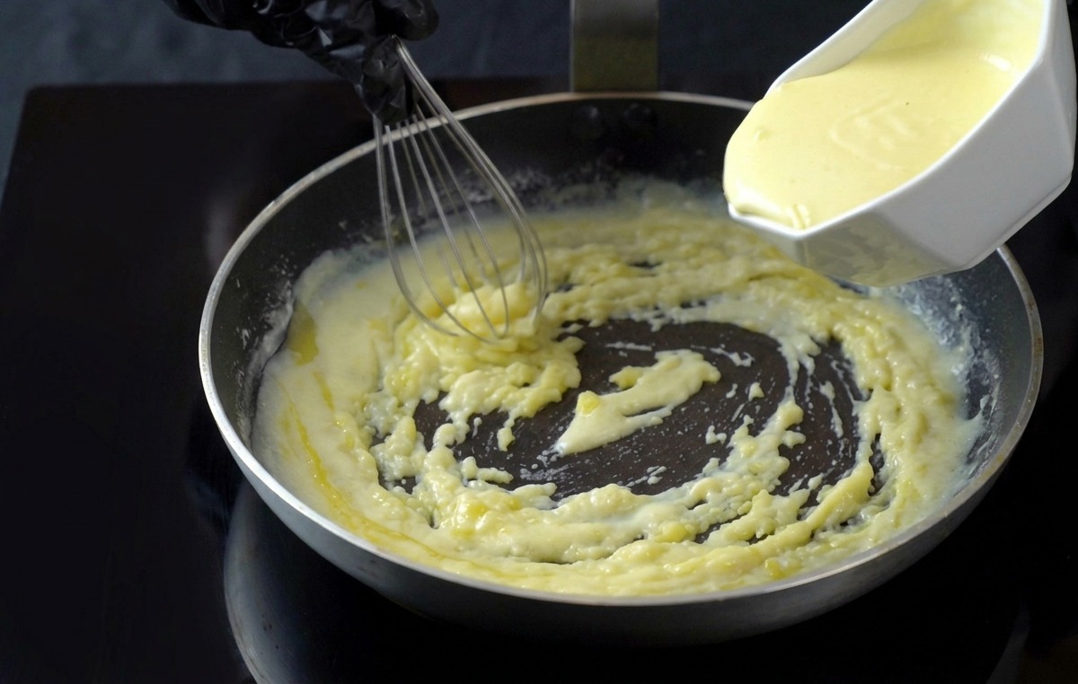 Sahne wird in die köchelnde weiße Sauce in der Pfanne gegossen und mit einem Schneebesen verrührt.